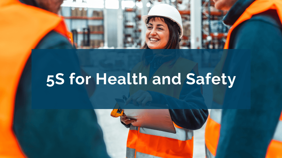 Smiling worker wearing a helmet and safety jacket, holding a clipboard, in a warehouse