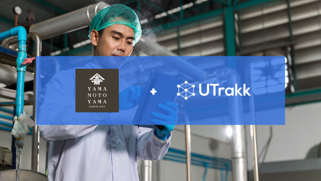 Worker wearing a hair net and white coat, standing in a factory while working on a tablet