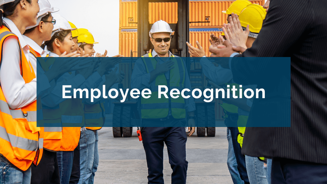 Employee wearing safety jacket and helmet, standing between two groups of workers, applauding, in an industrial setting