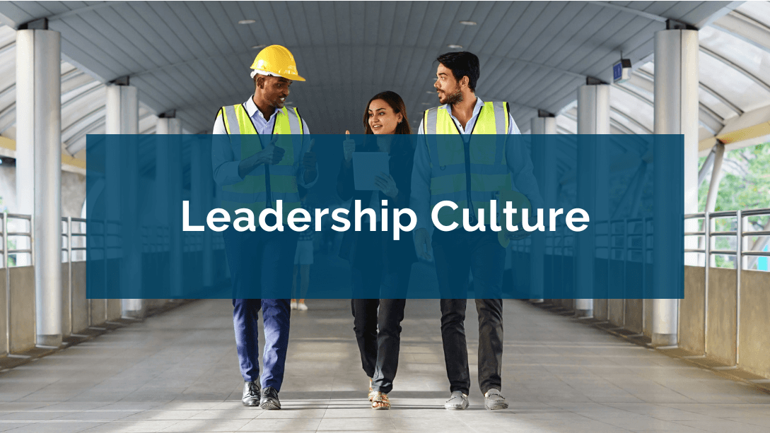 Three colleagues walking side by side, the two men wearing safety vests and helmets, and the woman in the center holding a tablet and giving a thumbs up