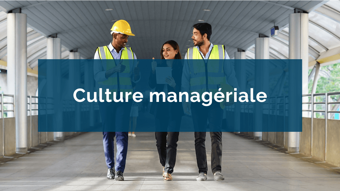 Trois collègues marchant côte-à-côte, les deux hommes portant des vestes et casques de sécurité et la femme, au centre, tenant une tablette et levant son pouce