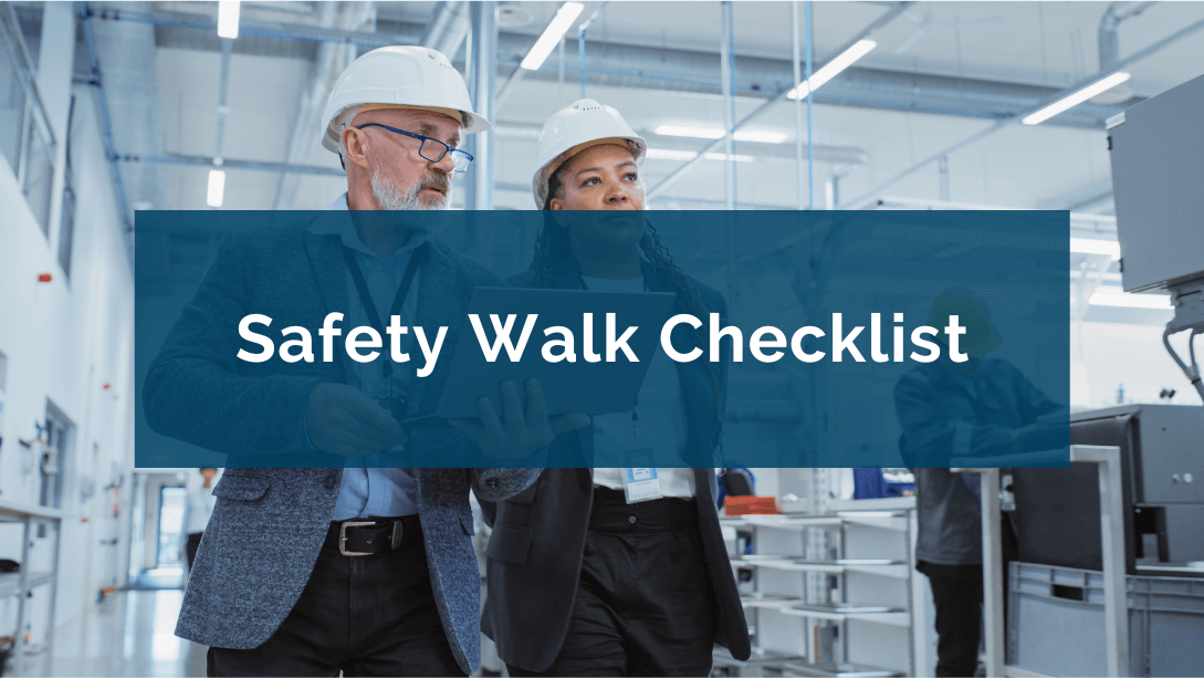 Two inspectors wearing safety helmets and walking in a factory, one holding an opened laptop in his hands