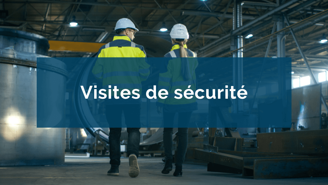 Deux travailleurs portant des casques et vestes de sécurité, vus de dos, se promenant sur le plancher d'une usine